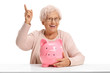 Joyful elderly woman with a piggybank pointing up