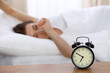 © rogerphoto - Beautiful sleeping woman resting in bed and trying to wake up with alarm clock