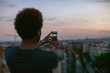 © BONNINSTUDIO/Stocksy - Back view of a young african american man taking a photo of Barcelona cityscape on his smartphone.