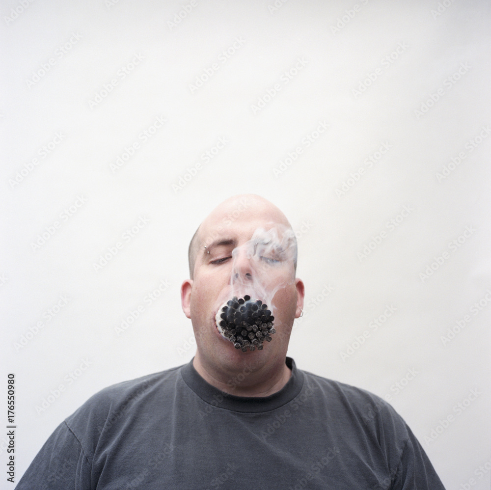 Overweight man with mouth full of lit cigarettes Stock Photo