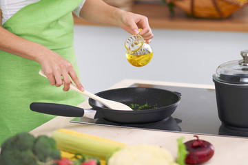 Young woman housewife cooking in the kitchen while adding olive oil. Concept of fresh and healthy meal at home