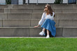 © papa - Stylish young woman in a long denim skirt sits on the steps of city stairs.