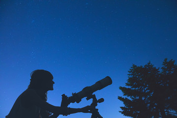 Wall Mural - silhouette of a girl while watching stars through the telescope in nature.