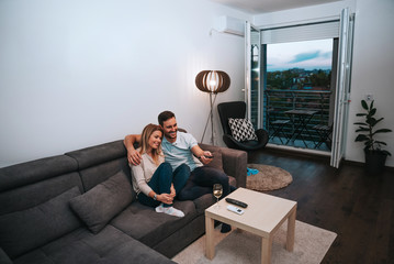 Wall Mural - Smiling young couple relaxing and watching tv at home.