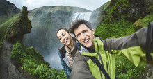 Smiling Couple, Man And Woman In Warm Clothes Making Selfie On A Skogafoss Waterfall Background, Iceland. Focus On The Man