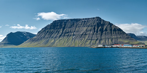 Wall Mural - Travel to Iceland. beautiful sunrise over the ocean and fjord in Iceland. Icelandic landscape with mountains, blue sky and green grass on the foreground. View of Flateyri, a village in the north-west