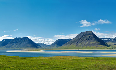 Wall Mural - Travel to Iceland. beautiful sunrise over the ocean and fjord in Iceland. Icelandic landscape with mountains, blue sky and green grass on the foreground. View of Flateyri, a village in the north-west