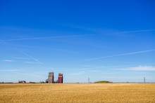 Two Old Abandoned Wooden Grain Storage Elevators With Two Old Buildings Beside It In A Golden Harvested Field In A Sunny Autumn Countryside Landscape