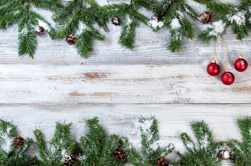 Wall Mural - Snowy Christmas branches with red ornaments on rustic white wooden background