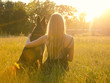 Blurred silhouette of a blonde girl embracing a German shepherd, sitting in the grass in the golden rays of the sun and looking at the sunset (selective focus on the girl), retro style