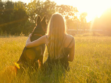 Blurred Silhouette Of A Blonde Girl Embracing A German Shepherd, Sitting In The Grass In The Golden Rays Of The Sun And Looking At The Sunset (selective Focus On The Girl), Retro Style