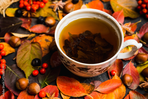 Plakat Filiżanka herbata z jesień liśćmi, dokrętkami, jagodami i pikantność na nieociosanym tle ,. Niewielka głębokość pola.