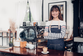 Poster - Asian female barista wear jean apron crossed her arms at counter bar with smile face,cafe service concept,owner business start up.