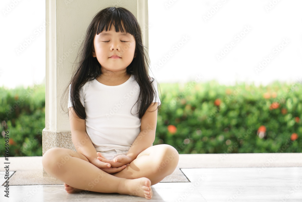 Asian children cute or kid girl sit for meditation with peace and relax in garden pavilion at temple or church and wearing white dress with sunlight on white with space - obrazy, fototapety, plakaty 