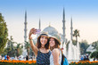 Two smiling girlfriends with smart phone doing selfie in front of the Blue Mosque in Istanbul. Travel and vacation in Turkey concept