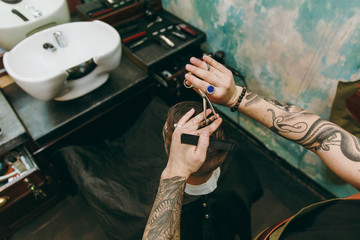 Close up shot of man getting trendy haircut at barber shop. Male hairstylist in tattoos serving client.