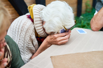 Portrait of old lady laughing hysterically hiding her face while playing card game with friends outdoors