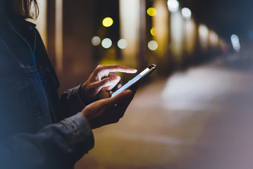 Wall Mural - Girl pointing finger on screen smartphone on background illumination glow bokeh light in night atmospheric city, hipster using in hands mobile phone, mockup glitter street, online internet concept