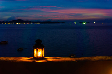 Wall Mural - The light or lantern is shining in the dark and placed on the edge of the mortar with sea and twilight sky at night as background.