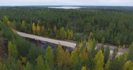 Wall Mural - Vehicle is on the autumn country road. Driving through the evergreen forest with lakes. Top view from drone. Karelia, Russia