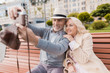 © Vadym Huzhva - A couple of retired people are sitting on a bench in the mall. They do selfie on an old film camera
