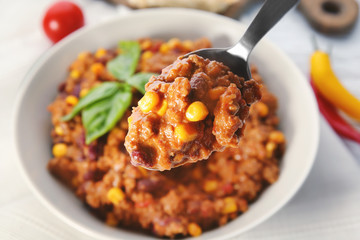 Wall Mural - Spoon with chili con carne over plate on table, closeup