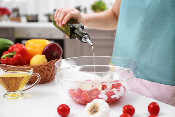 Wall Mural - Woman pouring olive oil onto vegetable salad in kitchen