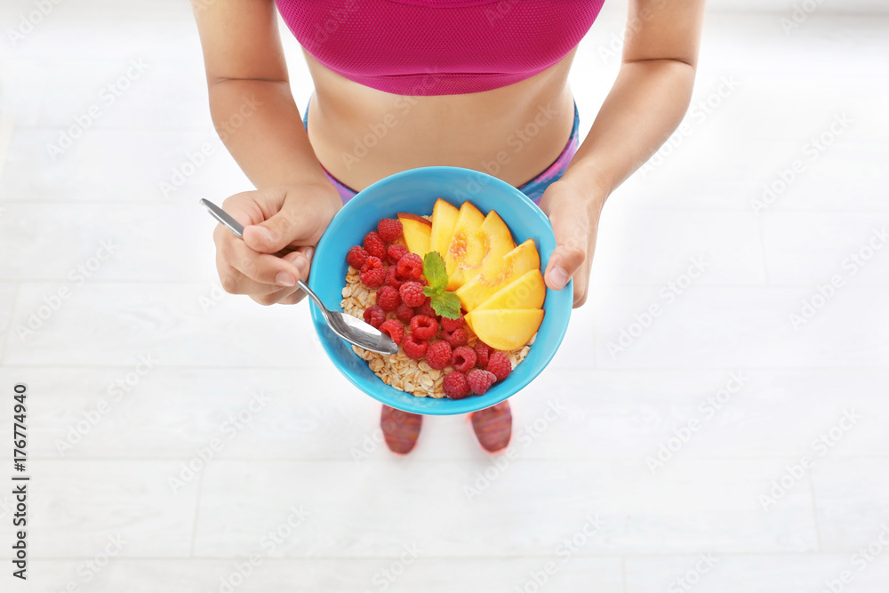 Young woman eating oatmeal on light background