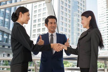 business man show thumb up and two business woman shaking hands for demonstrating their agreement to sign agreement or contract between their firms, companies, enterprises. success concept