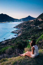 Woman Sitting Having A Drink Whilst Enjoying Dusk Overlooking A Beautiful Coastal Valley