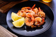 Skillet roasted jumbo shrimp on a black plate. Closeup. Shrimp roasted with sliced garlic and spices.