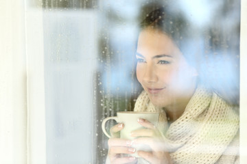 Wall Mural - Girl looking through a window holding coffee in winter