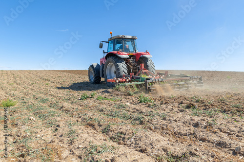 Zdjęcie XXL ciągnik rolniczy na pierwszym planie z niebieskim tle nieba.
