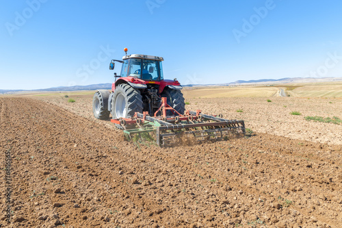 Zdjęcie XXL ciągnik rolniczy na pierwszym planie z niebieskim tle nieba.