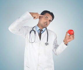 Male young doctor holding a red apple and gesturing head , health care idea