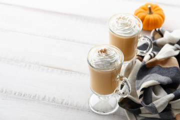 Wall Mural - Fall pumpkin spice latte with whipped cream and cinnamon, ornamental pumpkins and warm woolen scarf on white wooden background, copyspace