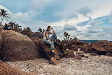 Wall Mural - boho styled young fashion model sitting on a stone at the beach