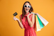© Drobot Dean - Close-up portrait of happy young brunette woman in sunglasses holding credit card and colorful shopping bags, looking at camera,