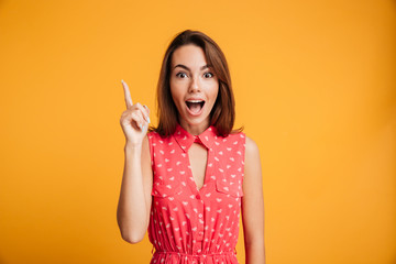 Sticker - Close-up portrait of amazed pretty young woman in red dress pointing with finger, looking at camera with open mouth