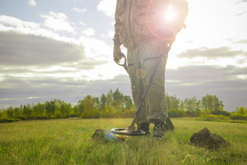 treasure hunter with a metal detector on a beveled wheat field in search of adventure against the backlight of the sun