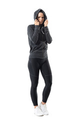 Wall Mural - Sporty woman in warm autumn sportswear with hoodie on head looking at camera. Full body length portrait isolated on white background.