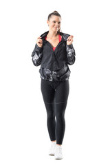 Wall Mural - Pretty active sportive woman in tracksuit hooded jacket smiling and looking away. Full body length portrait isolated on white background.