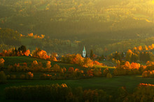 Evening In Kasperske Hory Church, Sumava, Czech Republic. Cold Day In Sumava National Park, Hills And Villages In Orange Trees, Misty View On Czech Landscape, Autumn Scene. Evening Landscape With Sun.