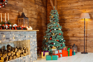 Photo of interior of room with a wooden wall, wreath and garlands, Christmas tree, fireplace with firewood. Christmas atmosphere. Home comfort