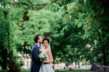 Wall Mural - Handsome groom and pretty bride with white bouquet stand on green lawn