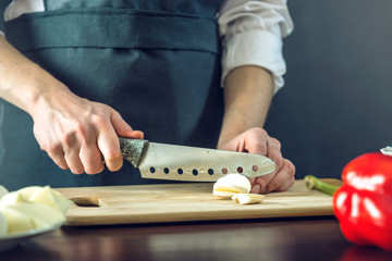 The chef in black apron cuts with a knife mozzarella cheese for pizza. Concept of eco-friendly products for cooking