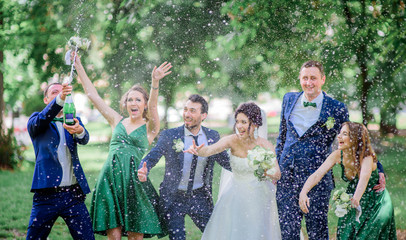 Wall Mural - Newlyweds and their friends open champagne bottle standing in the park