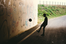 Silhouette Of A Boy Kicking A Ball Against A Tunnel Wall.
