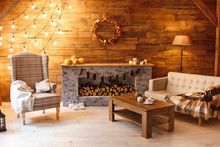 Home Comfort. Armchair Near The Fireplace With Firewood. Photo Of Interior Of Room With A Wooden Wall, Wreath And Garlands, Christmas Atmosphere