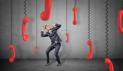 Wall Mural - a scared businessman on concrete background hides from many red retro phone receivers hanging down o